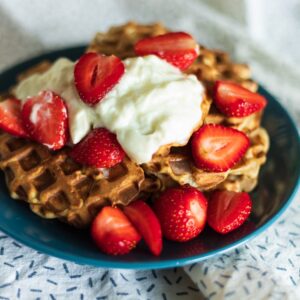 a blue plate topped with waffles covered in whipped cream and strawberries